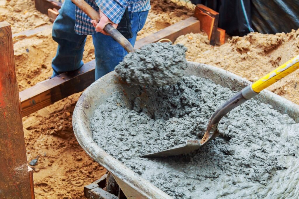 A person shoveling fresh cement mix from a wheelbarrow at a construction site.
